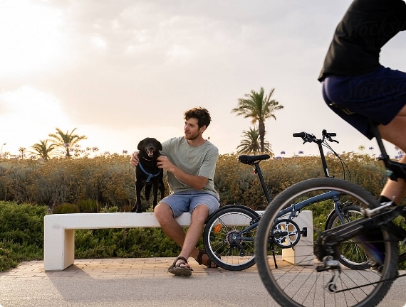 Homme assis sur un banc de parc avec son chien et des vélos passant
